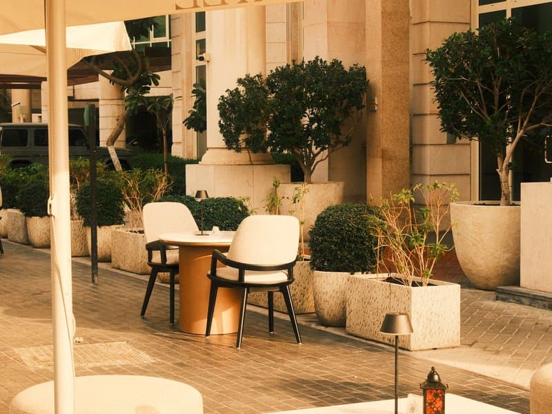 Outdoor cafe setting with white chairs and a round table surrounded by potted plants.