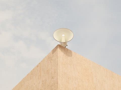 A large speaker mounted on a beige wall under a cloudy sky.