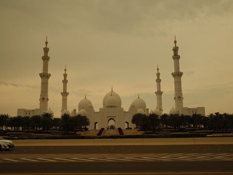 A grand mosque with multiple domes and minarets under a cloudy sky.
