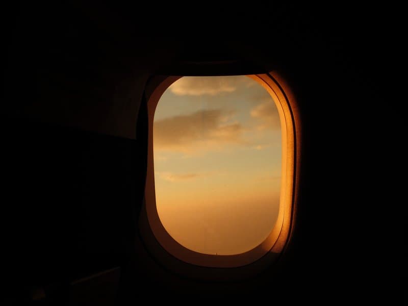 Airplane window view at sunset with orange and blue hues in the sky.