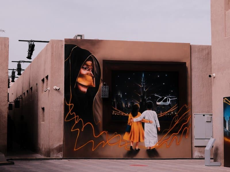 A colorful mural depicting two children walking towards a starry night, with a large face in the background.
