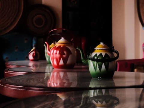 Colorful teapots arranged on a glass table in a dimly lit indoor setting.