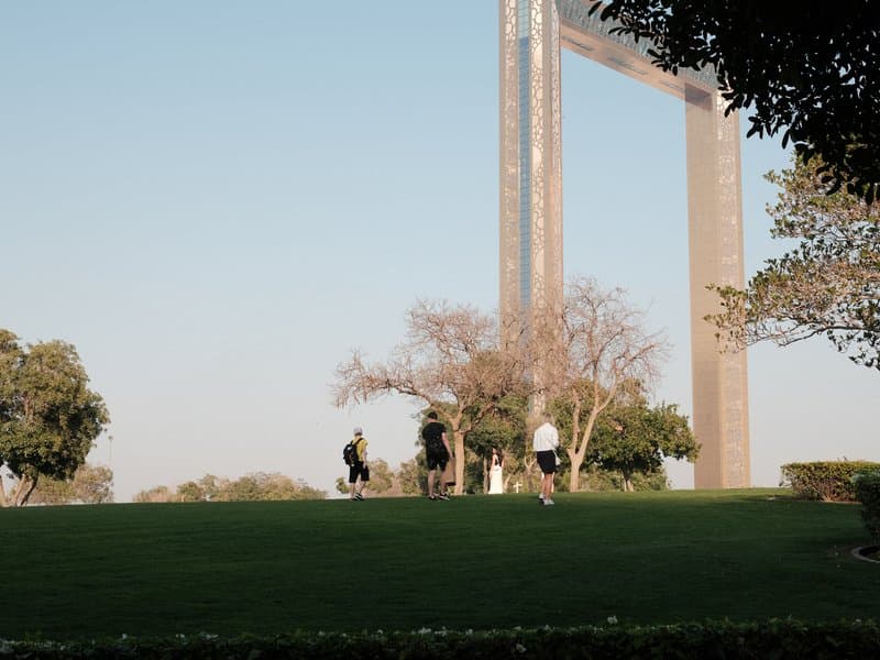 Three people walking on a grassy area with a large metal frame structure in the background.