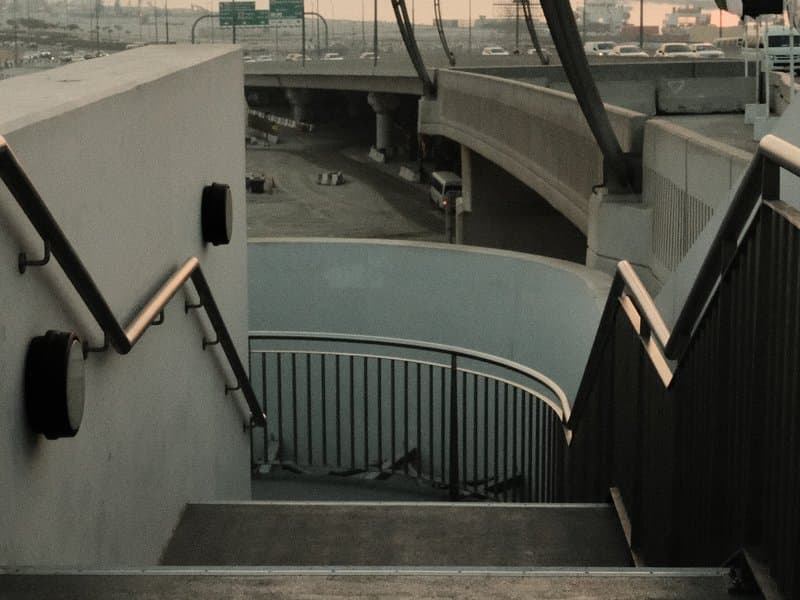 A modern staircase leading down with curved walls and urban infrastructure in the background.