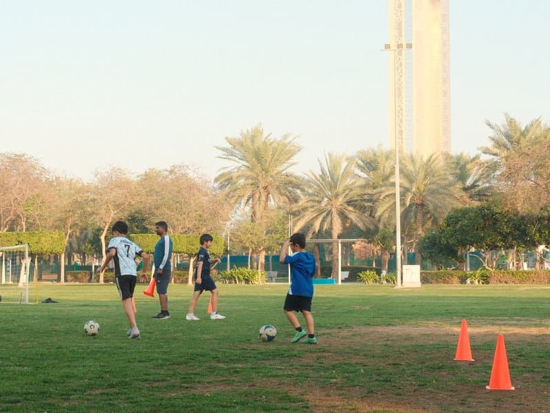Four young players practicing soccer on a grassy field with palm trees in the background.