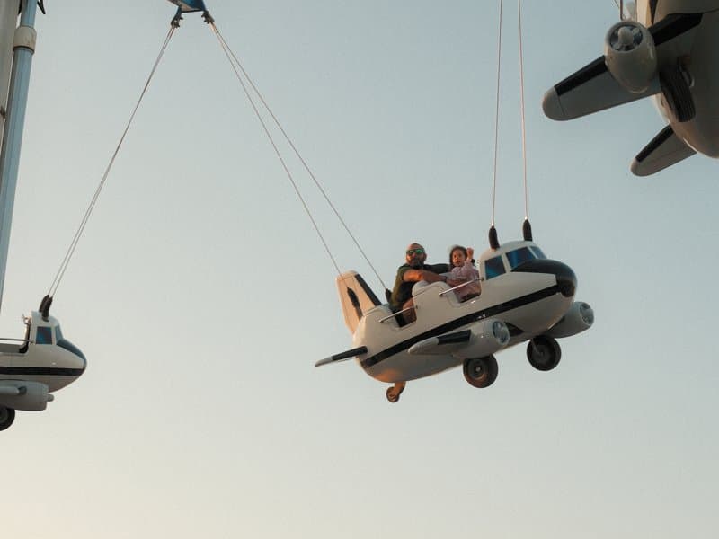 Two toy airplanes suspended in the air with figures inside, against a soft sunset sky.