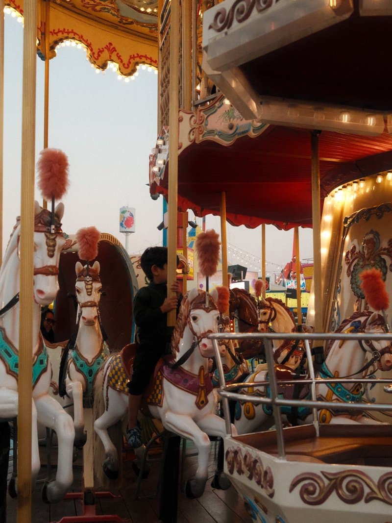 A child climbing onto a carousel with ornate horses, colorful decorations, and bright lights.