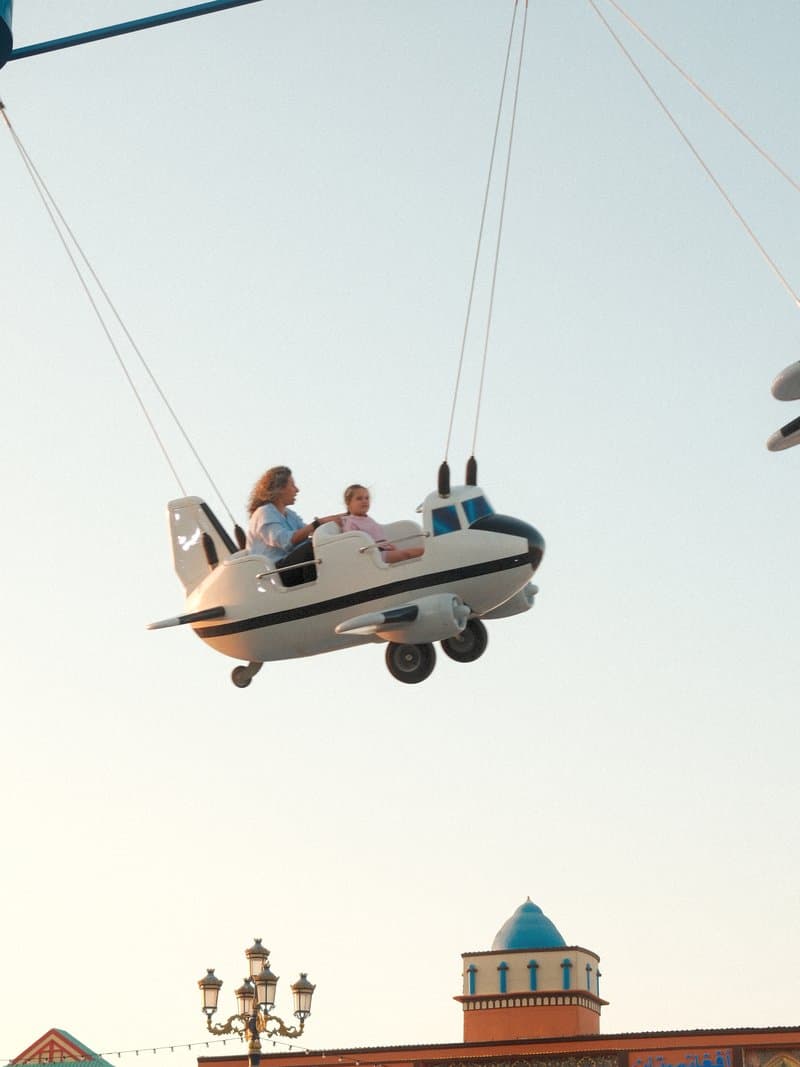Two children enjoying a ride in a toy airplane suspended in the air against a clear sky.