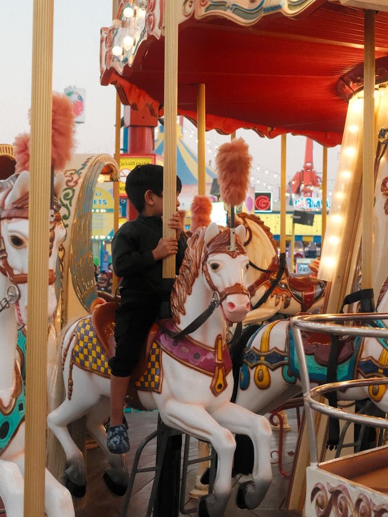 A child riding a carousel horse at a carnival, surrounded by colorful lights and decorations.