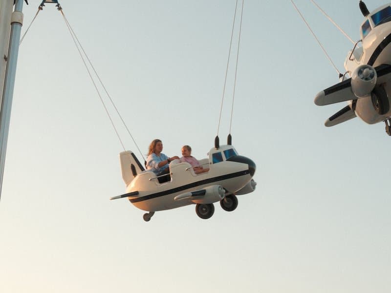 Two children enjoying a ride in a small airplane at an amusement park during sunset.