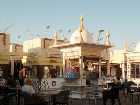A vibrant outdoor market scene with stalls and a decorative pavilion under a clear blue sky.