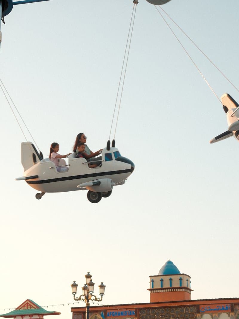 Two children enjoying a ride in a small airplane at an amusement park against a clear sky.