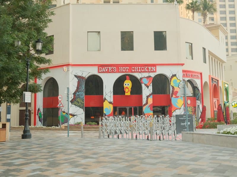 Colorful mural on a building with artistic designs and a tiled plaza in front.