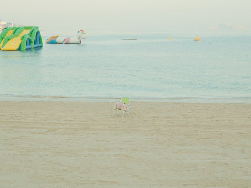 A small dog running on a sandy beach near calm water with inflatable structures in the background.