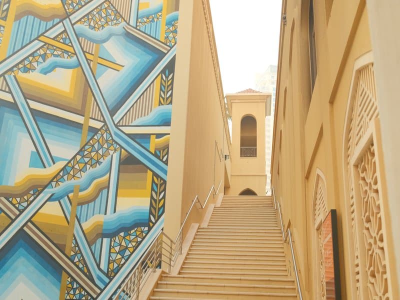 Staircase leading up between buildings with a colorful mural on the left side.