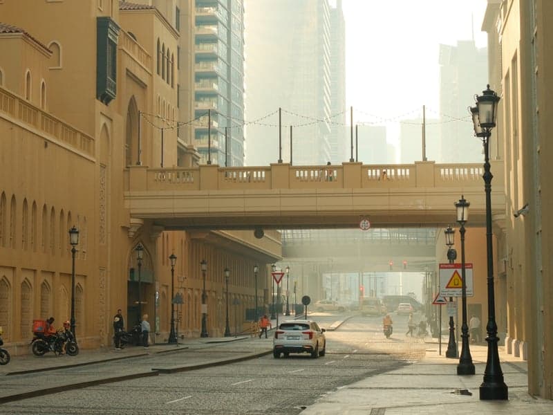A quiet urban street with a yellow building and a bridge overhead, shrouded in morning haze.