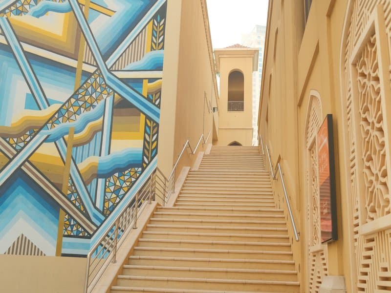 Staircase leading up with a colorful mural on the left side and a building in the background.