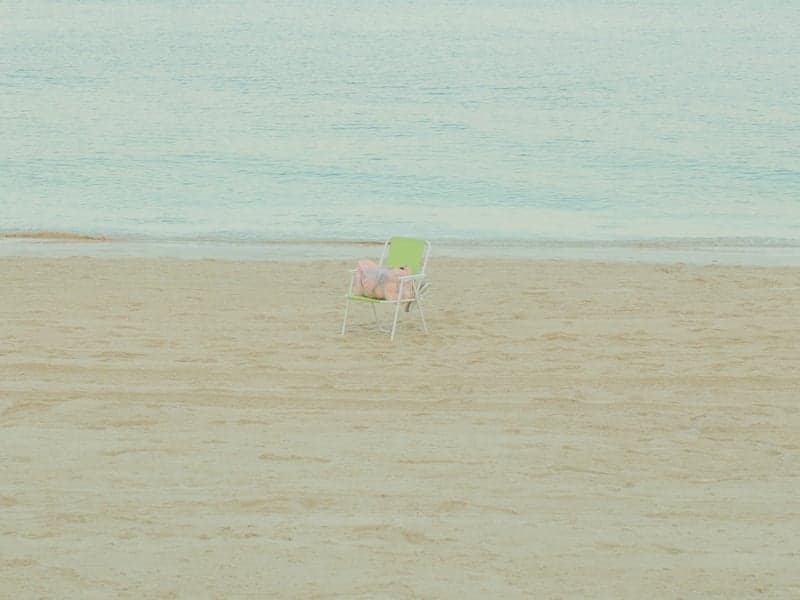 A solitary beach chair on a sandy shore with gentle waves in the background.