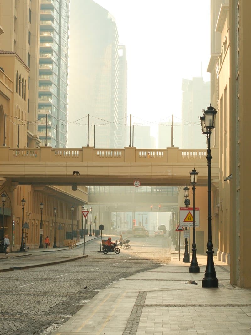 A quiet urban street with a bridge overhead, soft light filtering through tall buildings in the background.