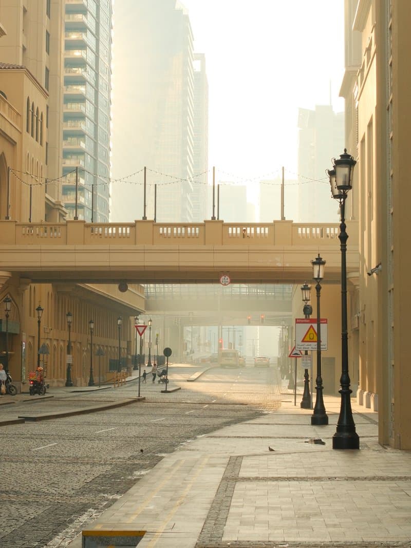 A quiet urban street with a bridge in the background, shrouded in morning mist and soft light.