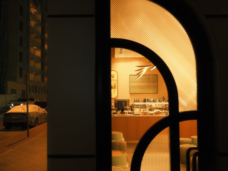 A warm-lit interior visible through an arched window at night, with a glimpse of a street outside.