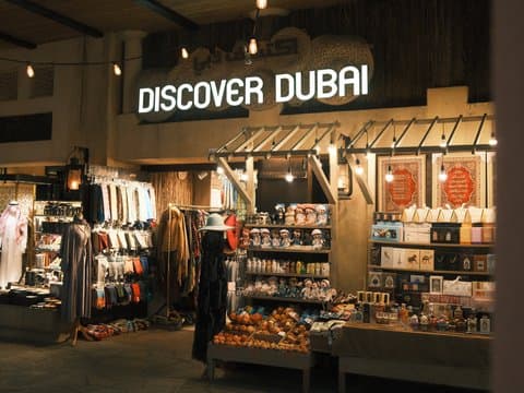 A shopfront displaying souvenirs and local products with a sign that reads 'Discover Dubai'.