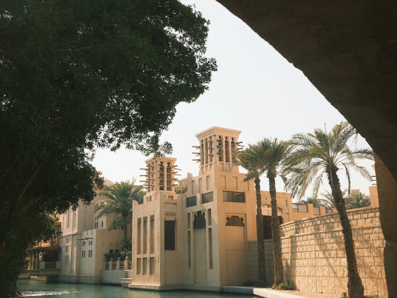 Architectural structure with palm trees and waterway under a sunny sky.