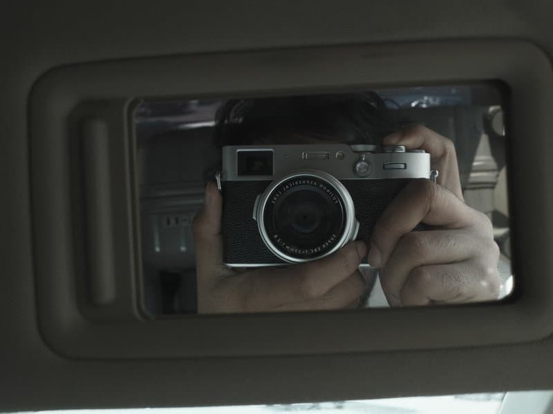 A reflection of a person holding a camera in a car's rearview mirror.