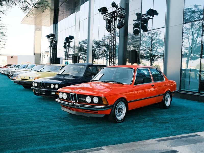 A row of vintage BMW cars displayed outdoors in front of a modern glass building.