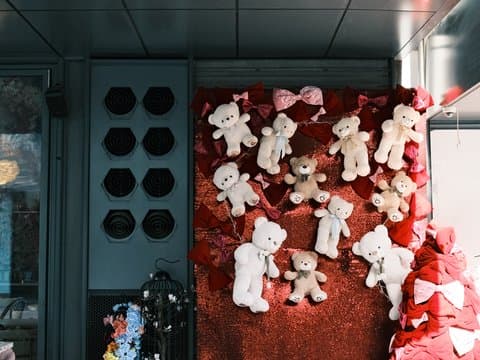 A display of teddy bears on a red backdrop with decorative elements and hats in the background.