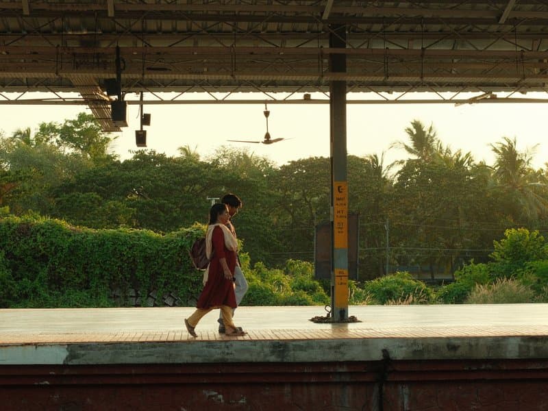 A woman walking on a train platform during golden hour with lush greenery in the background.