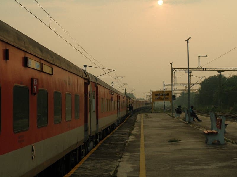 A train at a quiet station during sunset with a hazy sky and a few people in the background.
