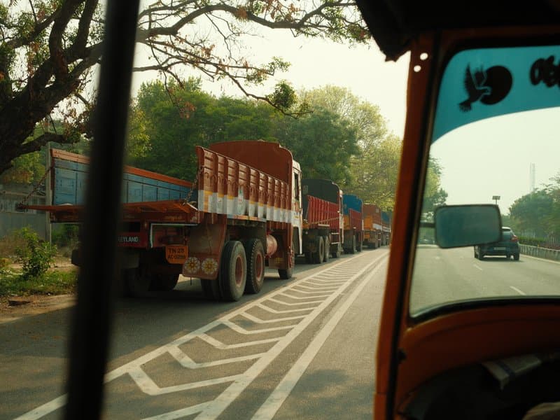 View from a vehicle showing a line of trucks on a road with trees in the background.