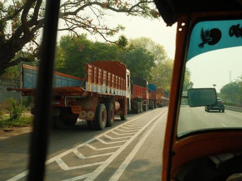 View from a vehicle showing a line of trucks on a road with trees in the background.
