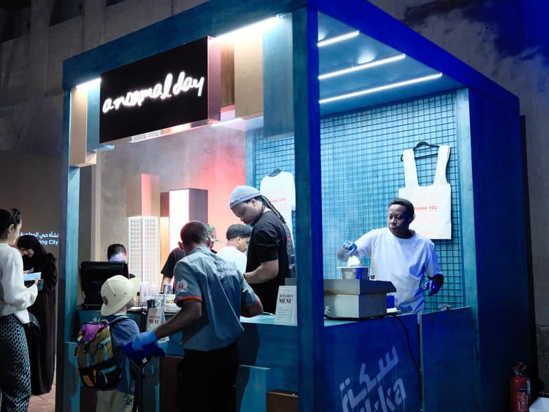 A vibrant food stall at night with people ordering and staff preparing food in a blue-lit environment.