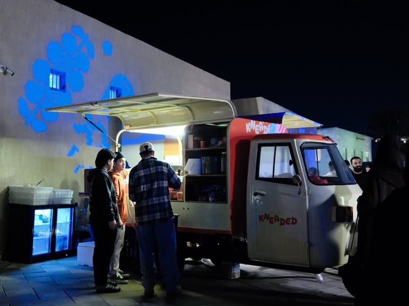Food truck at night with customers ordering, illuminated by soft light against a dark background.