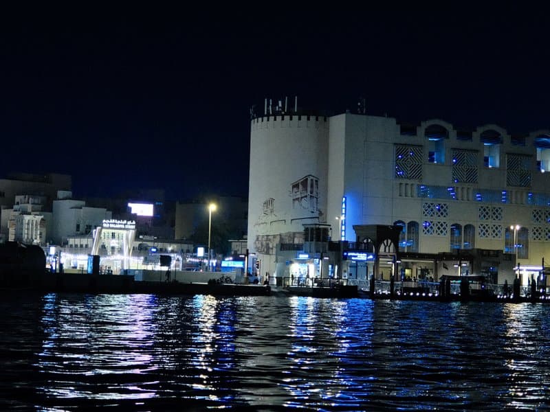 Night view of a waterfront with illuminated buildings and reflections on the water.