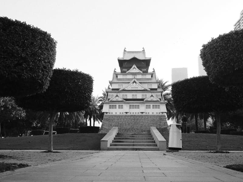 A traditional Asian-style building surrounded by manicured trees in a park setting.