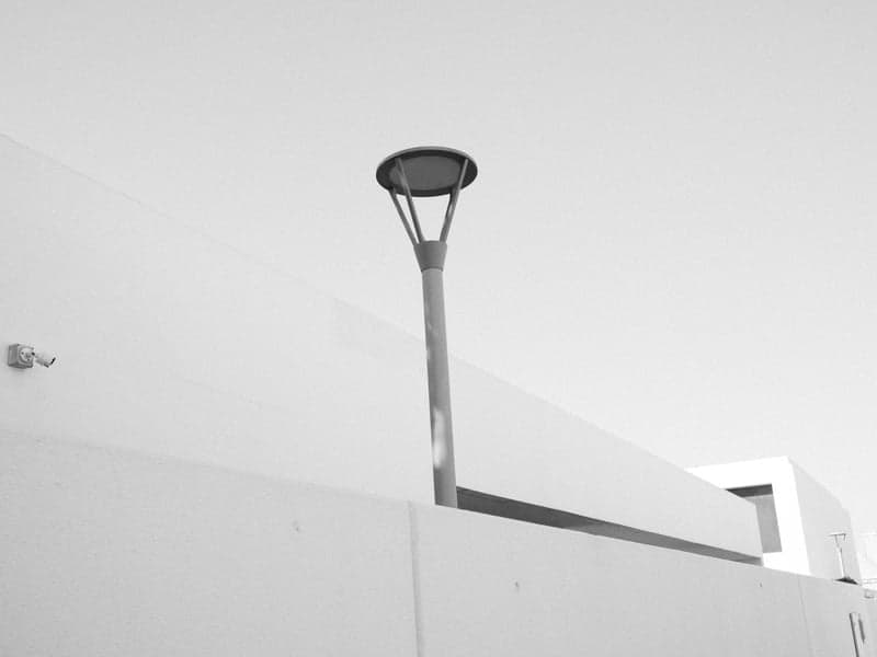 A minimalist urban scene featuring a tall street lamp against a stark white wall.
