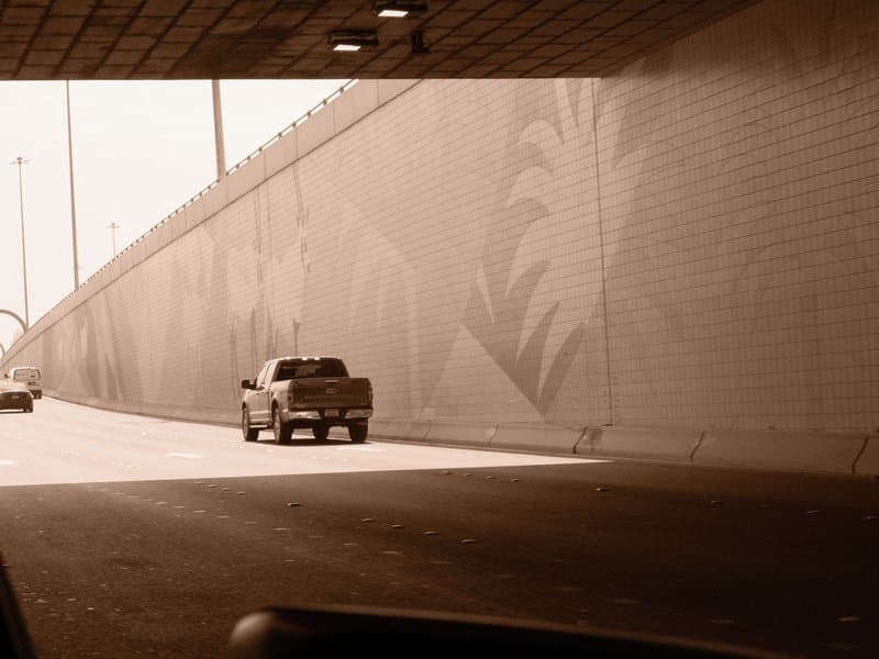 A truck driving through a tunnel with a patterned wall and bright light at the tunnel's exit.