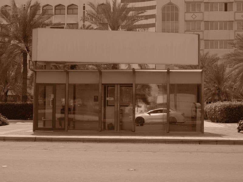 A vintage-style storefront with a blank sign, surrounded by palm trees and urban buildings.