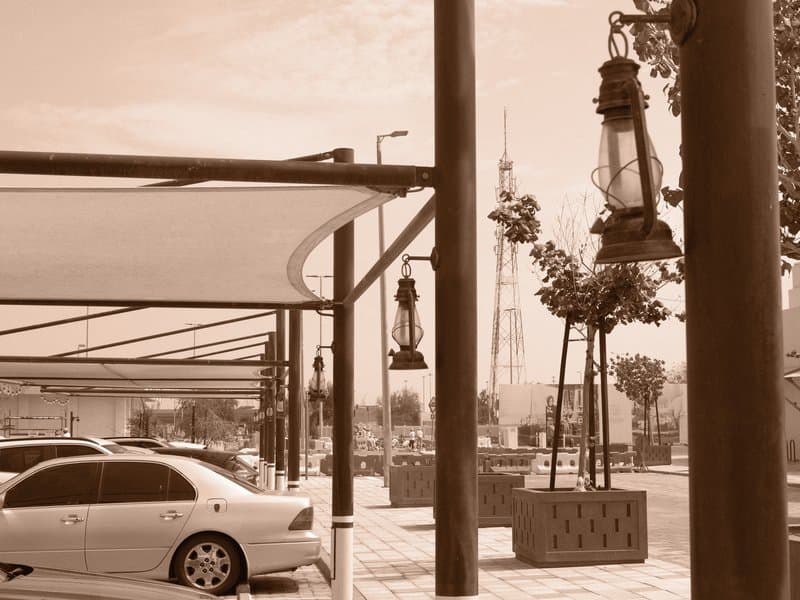 A sepia-toned view of a parking area with vintage lanterns, cars, and distant buildings.