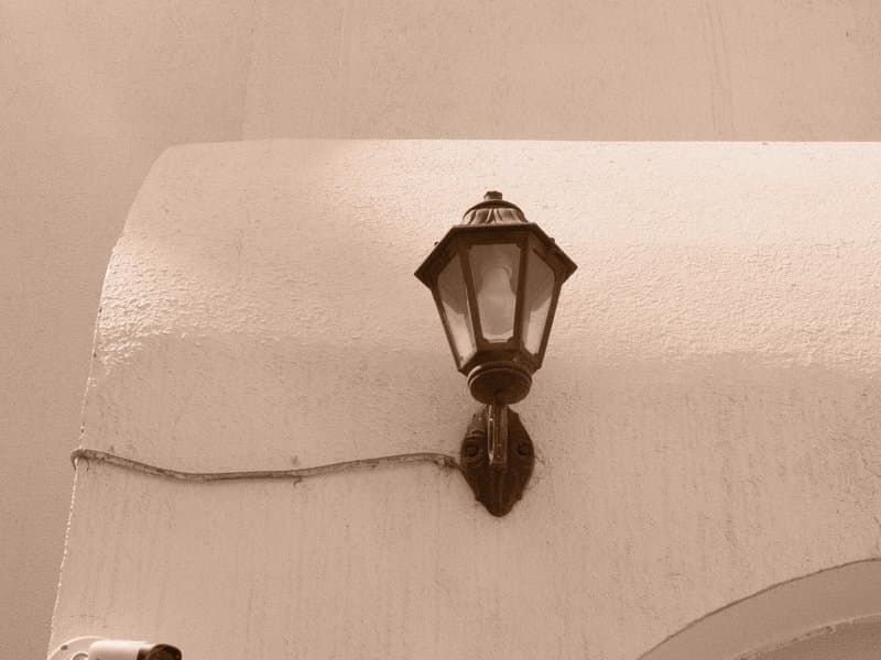 A vintage lantern mounted on a white wall, with a textured surface and soft lighting.