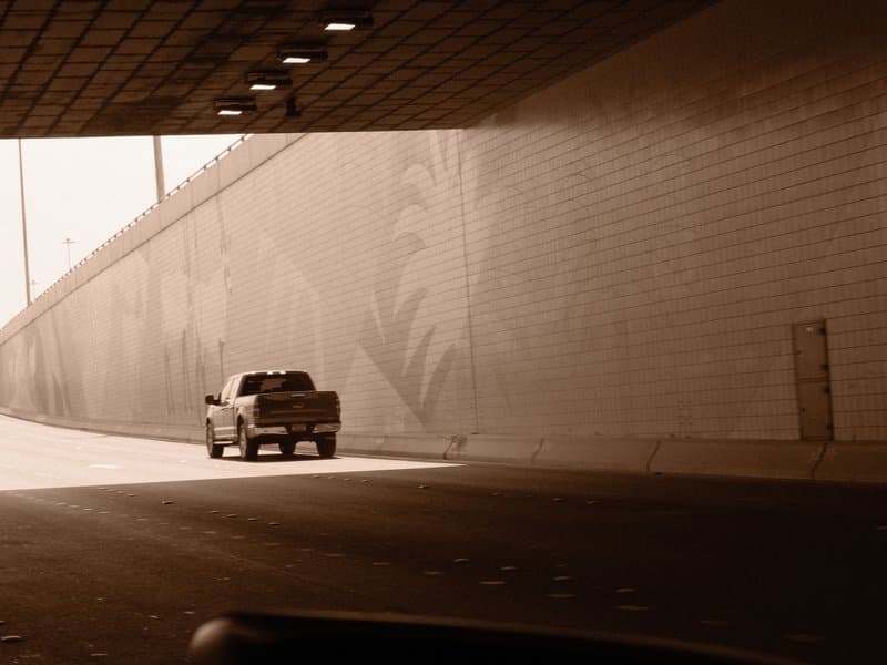 A truck driving through a tunnel with a patterned wall, creating a dramatic light contrast.