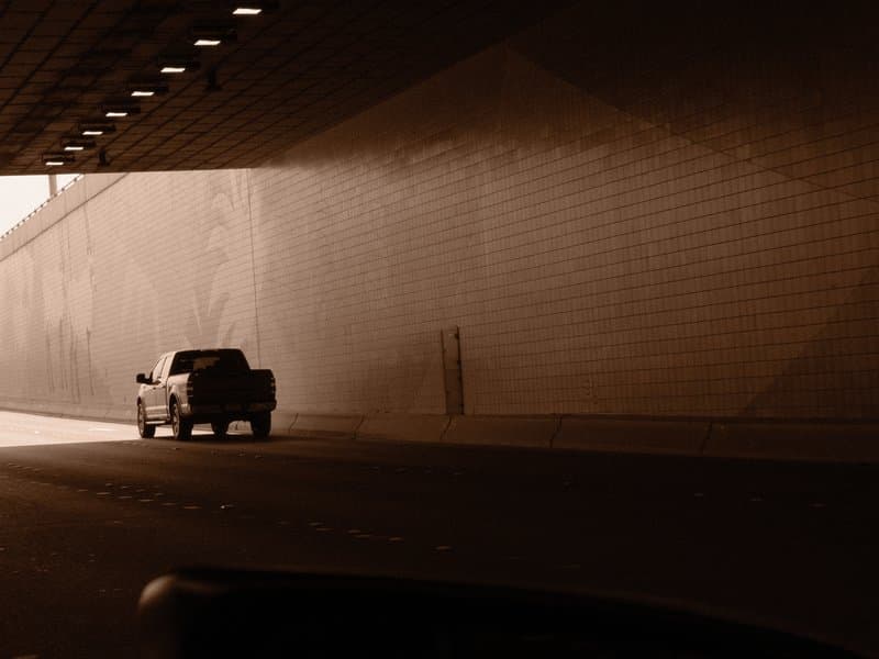 A truck exiting a tunnel with light illuminating the entrance, creating a dramatic contrast.
