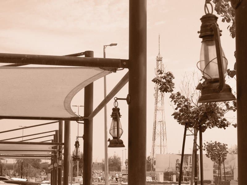 A sepia-toned image of lanterns hanging from a structure with a tower in the background.