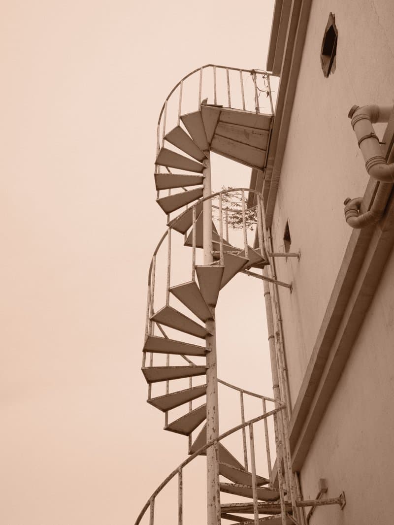 A spiral staircase ascending the side of a building against a pale sky.