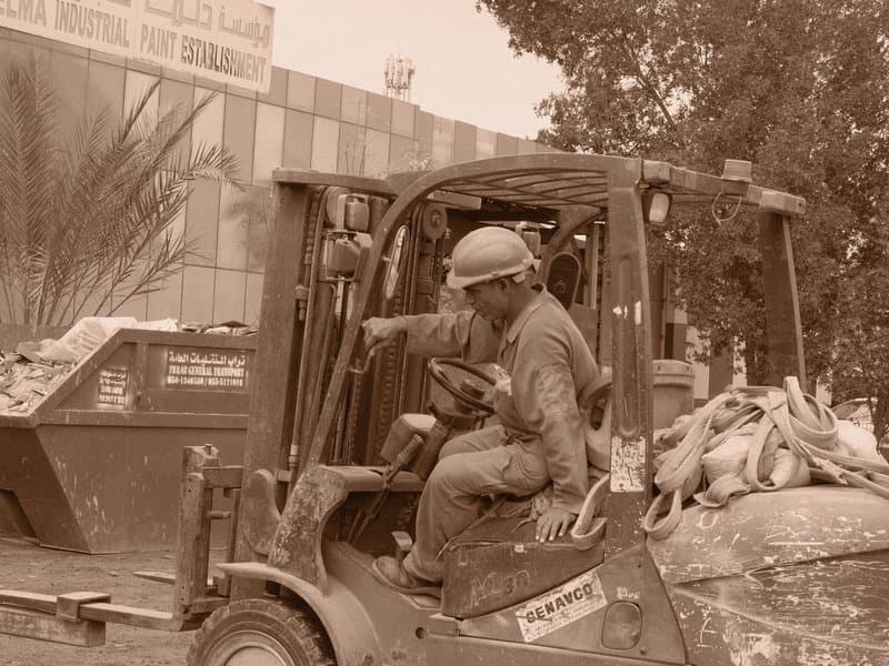 A construction worker operating a forklift in front of a building, surrounded by debris and tools.