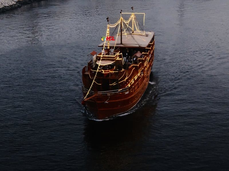 A wooden boat adorned with lights gliding through dark water, surrounded by a serene atmosphere.