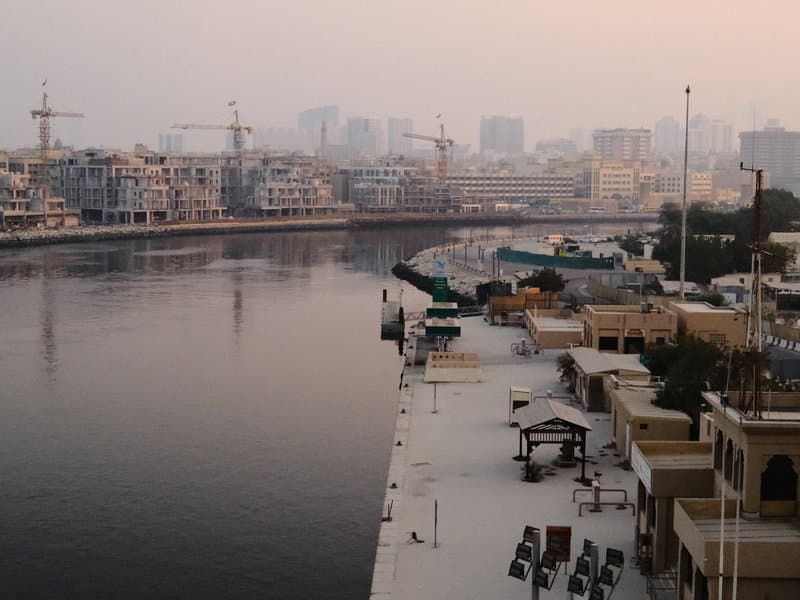 View of a river with buildings and cranes in the background during twilight.